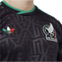 Close-up of a black Mexico national football team jersey with a subtle geometric pattern, featuring the team crest and a green, white, and red Adidas trefoil logo.