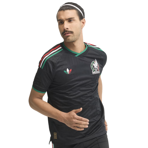A man with a mustache in a running pose wears a black Mexico national team soccer jersey and a white headband against a white background.