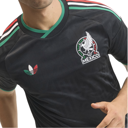 Close-up of a person wearing a black Mexico football jersey with green, white, and red accents, the national team crest, and a colorful Adidas trefoil logo.