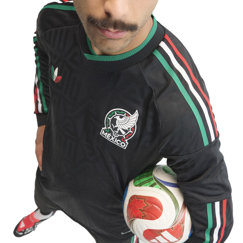 High-angle shot of a man with a mustache wearing a black Mexico soccer jersey and holding a soccer ball against a white background.