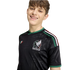 A smiling young person wearing a black Mexico national football team jersey with green accents and the official team crest, set against a plain white background.