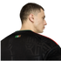 Rear profile of a man wearing a black Mexico soccer jersey with red shoulder stripes and "SOMOS MÉXICO" on the back neck.