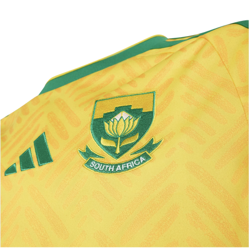 Close-up of a yellow South Africa sports jersey with a green embroidered crest featuring a King Protea flower and "SOUTH AFRICA" text.