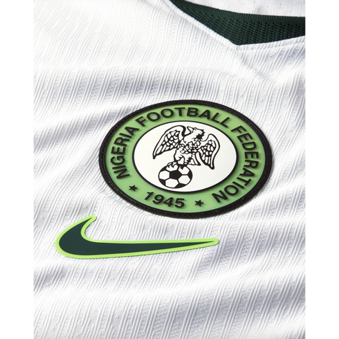 Close-up of a white Nigeria football jersey featuring the Nigeria Football Federation crest and a green Nike swoosh logo on textured, ribbed fabric.