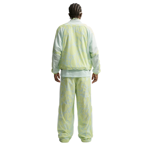 Rear view of a person with braided hair in a light green and yellow marbled-print tracksuit. The loose-fitting jacket and pants feature mesh paneling on the sleeves and sides.