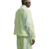 A person wearing a lime green and light blue abstract patterned tracksuit with mesh panels and sporty sunglasses, seen from the back against a white background.