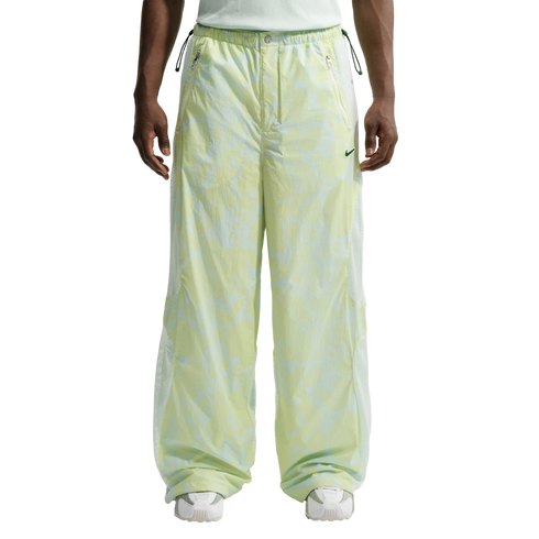 A front view from the waist down of a person wearing baggy, light green and white patterned Nike track pants with white mesh side panels and white sneakers.