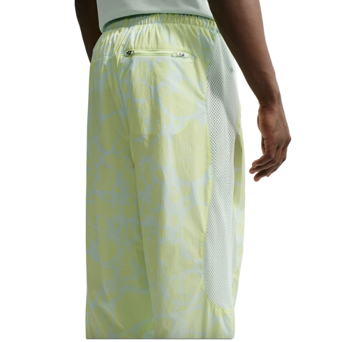 Rear view of a person wearing light green patterned athletic pants featuring white mesh side panels, an elastic waistband, and a small zippered back pocket.