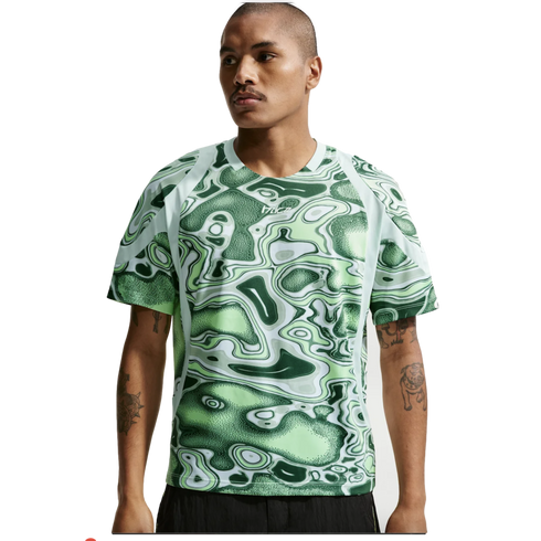 A man wearing a green and white abstract-patterned t-shirt with raglan sleeves and black shorts against a white background.