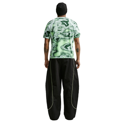 Back view of a person in a green patterned tee and baggy black pants with neon piping, against a white background.