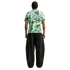 Back view of a person in a green patterned tee and baggy black pants with neon piping, against a white background.