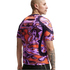 Rear view of a man wearing a Nike shirt with a vibrant, abstract purple and orange pattern. He has a bald head and arm tattoos, set against a plain white background.