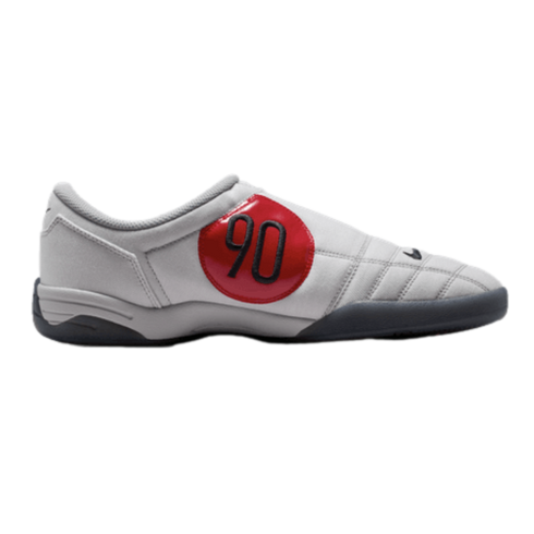 Side profile of a grey Nike Total 90 indoor soccer shoe with a large red circular patch featuring a black "90" and a dark grey sole.