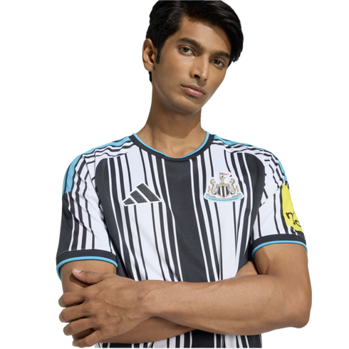 A man posing with arms crossed in a black and white striped Adidas Newcastle United soccer jersey.