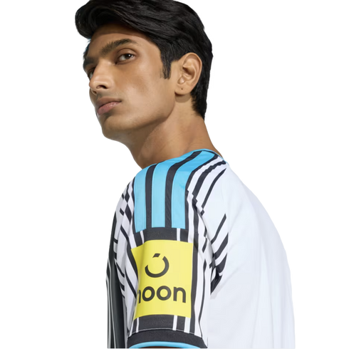 Side profile of a man wearing a white and black striped jersey with a light blue shoulder panel and a yellow 'noon' logo patch on the sleeve.
