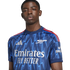 Portrait of a young Black man wearing a blue Arsenal football jersey with a zigzag pattern, posed against a black background.
