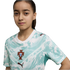 A young girl with dark hair tied back wears a white and teal patterned Portugal national football team jersey with the FPF crest and dark red Puma logos. She looks directly at the camera against a solid black background.