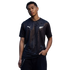 A young man poses against a black background, wearing a black Puma t-shirt featuring a tonal fern pattern and the white New Zealand Silver Fern logo.