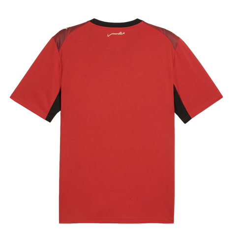 The back view of a red short-sleeved athletic jersey featuring a black collar, maroon shoulder panels, and black accents under the sleeves. A small, white Arabic script logo is centered below the back of the neck.
