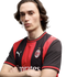 A man with shoulder-length brown hair and arms crossed, wearing a red and black AC Milan soccer jersey with a white Puma logo against a plain white background.