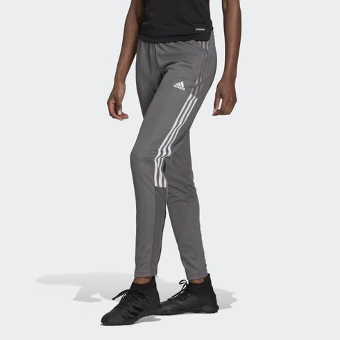 A person wearing gray Adidas tracksuit pants with three white stripes and black sneakers.