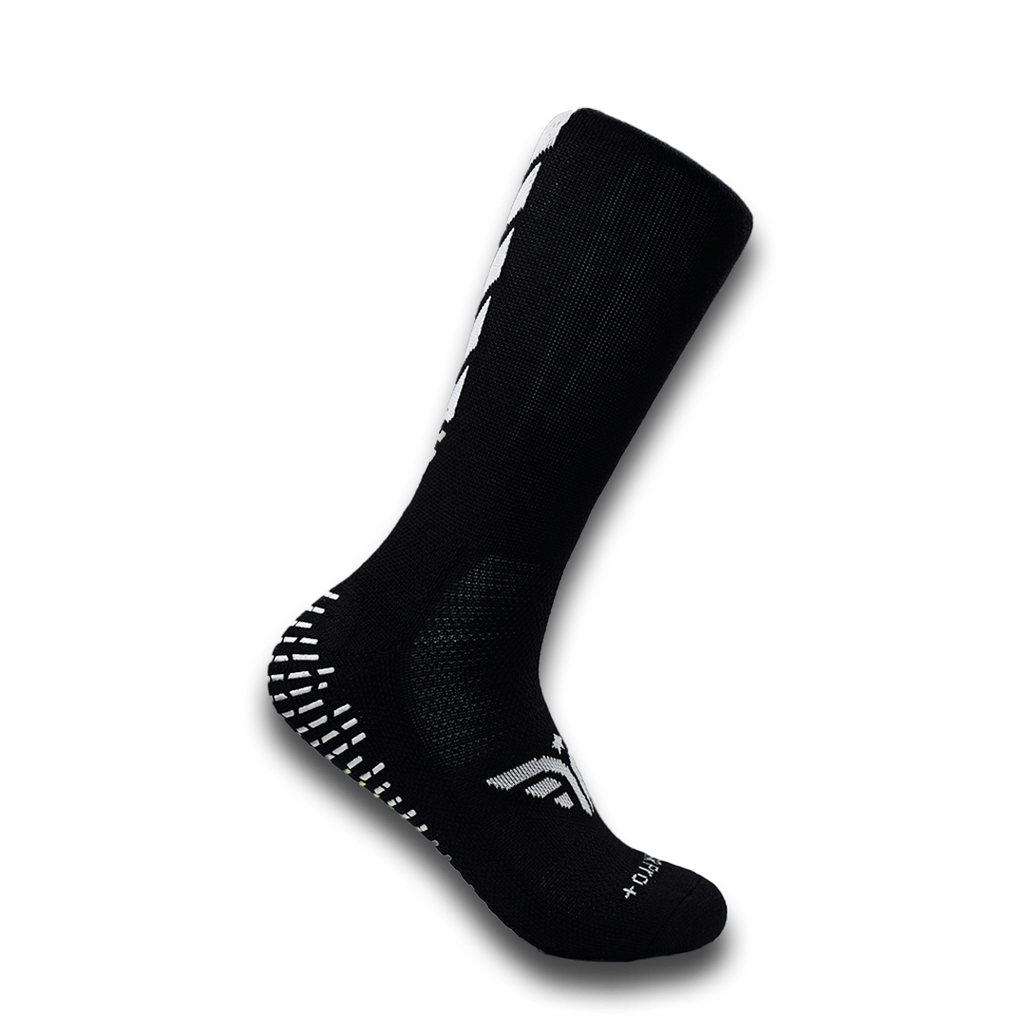 A black For The Footballer XLR8R Pro No Slip Sock featuring white logo details and rubberized grip pads on the heel and sole.