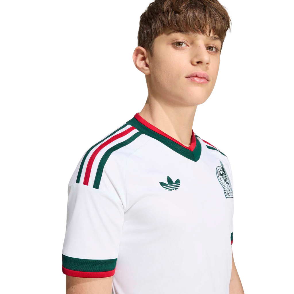 A young man wearing a white Mexico football jersey with green and red trim, an Adidas logo, and team crest, set against a black background.