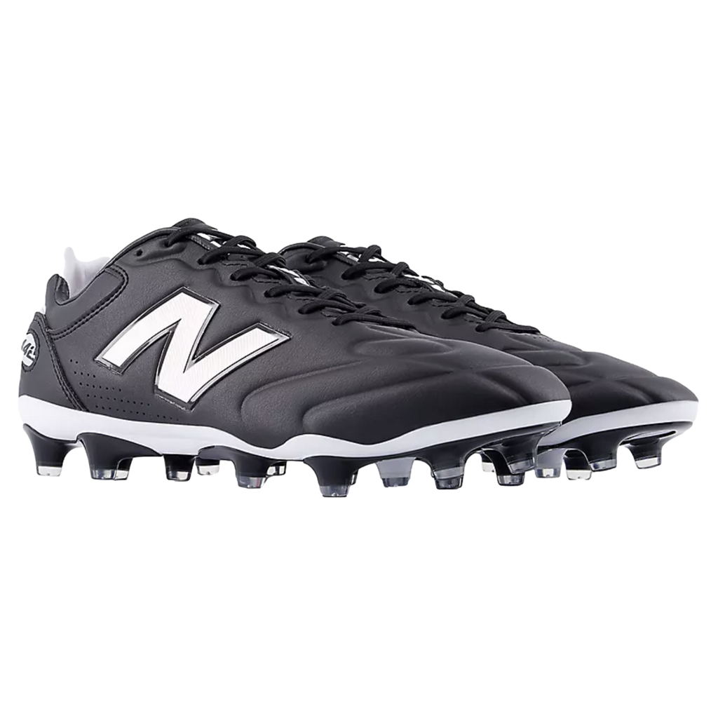 A pair of black and white New Balance soccer cleats featuring the iconic white "N" logo on the side and a studded outsole, set against a black background.